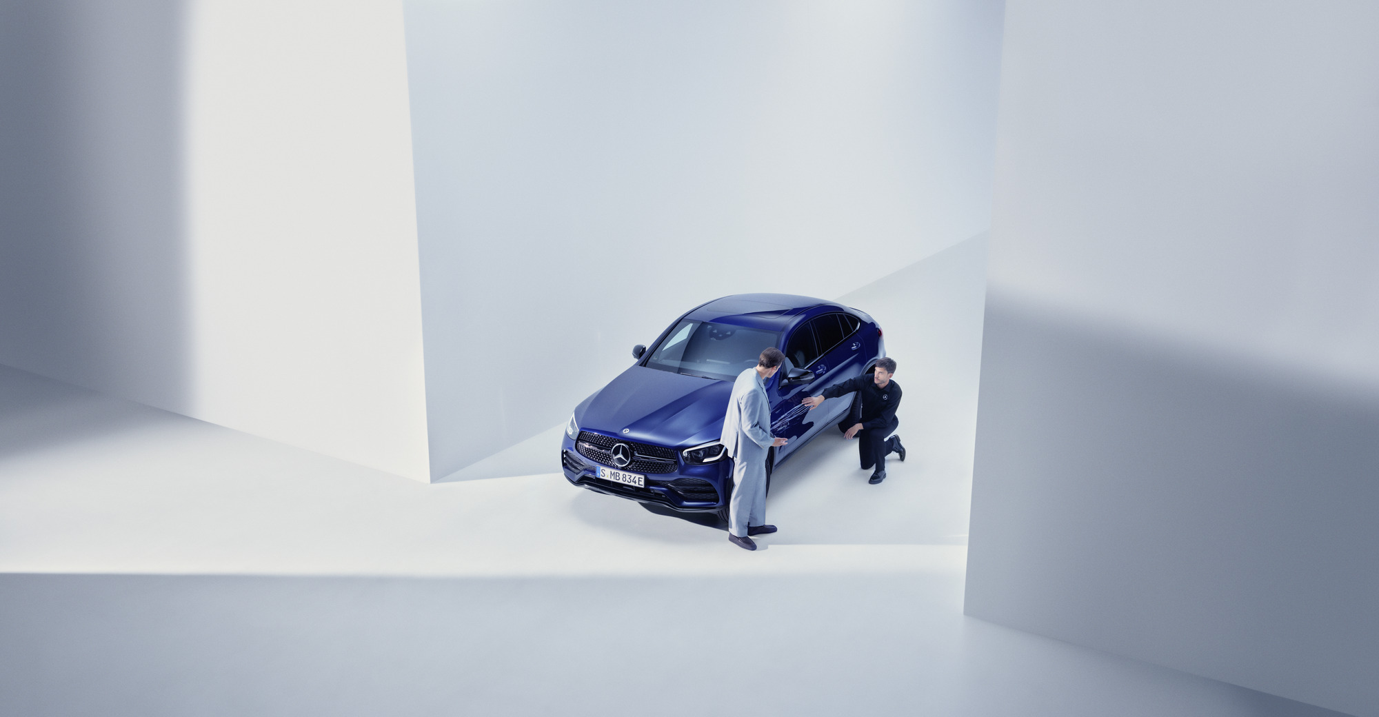 Asistencia en carretera y en caso de daños | Mercedes-Benz Hombre del equipo de apoyo de Mercedes-Benz arrodillado junto a un Mercedes-Benz averiado