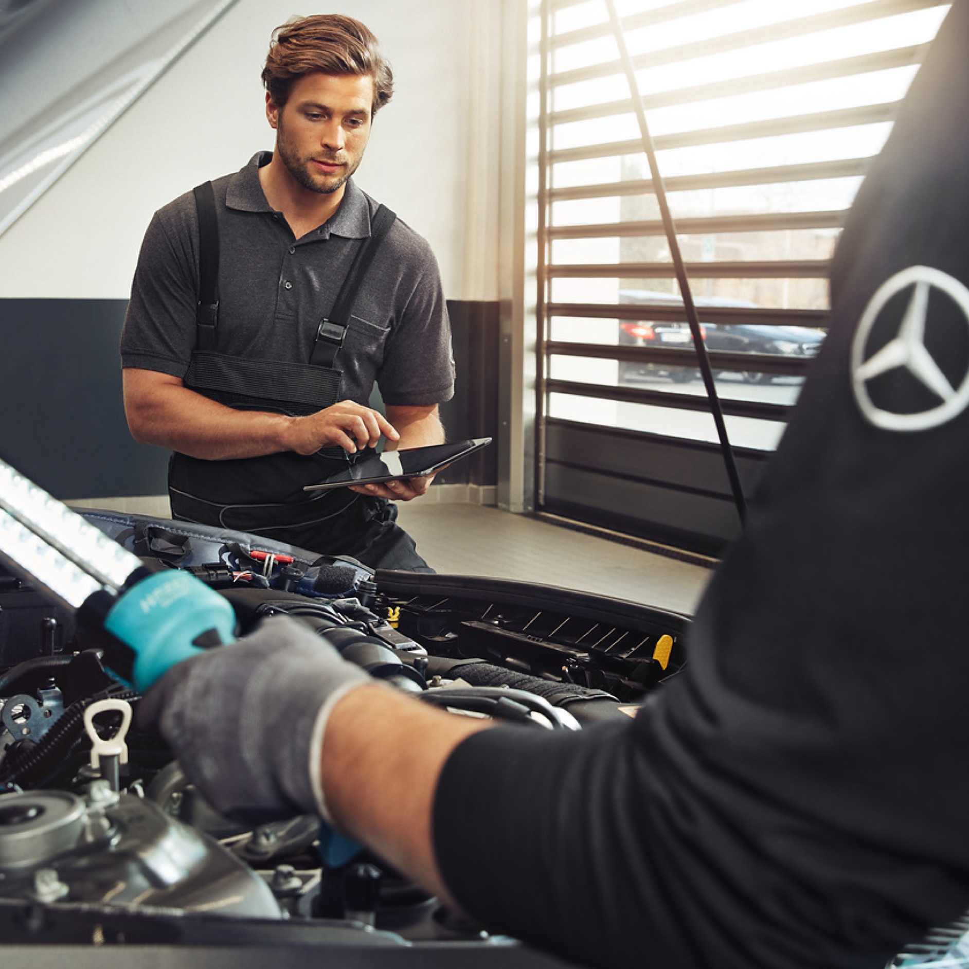 Recambios originales Dos técnicos de Mercedes-Benz examinan el compartimento del motor de un vehículo.